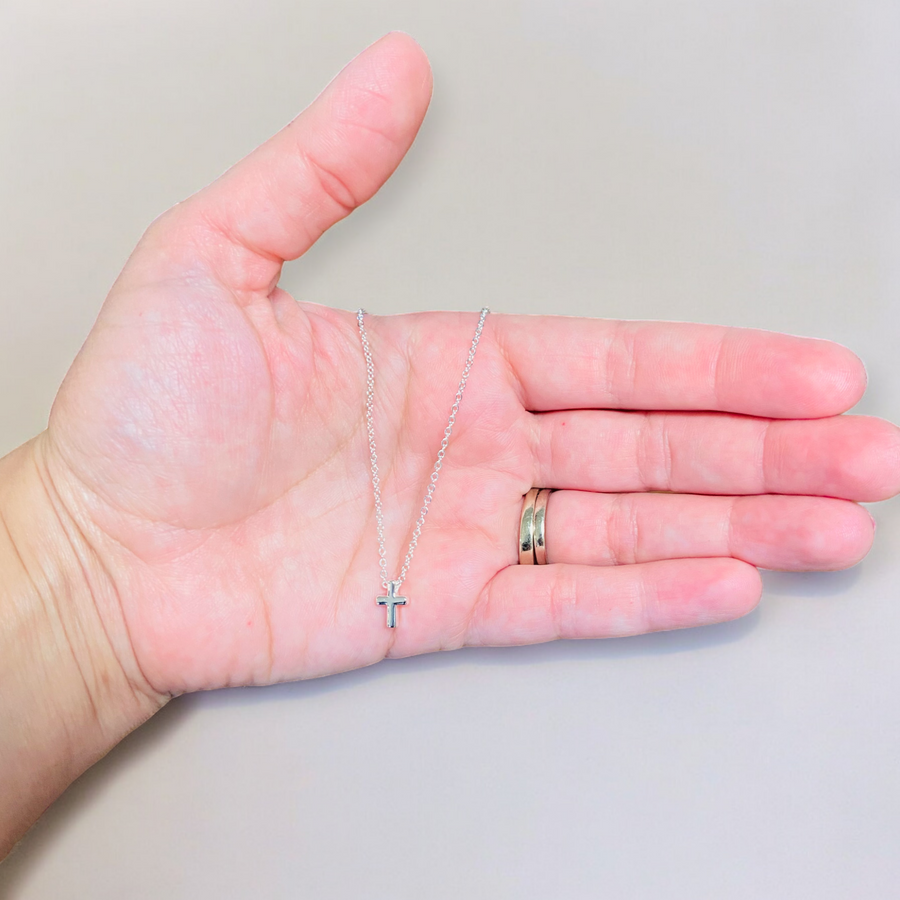 Silver dainty necklace with a small cross pendant held in one hand